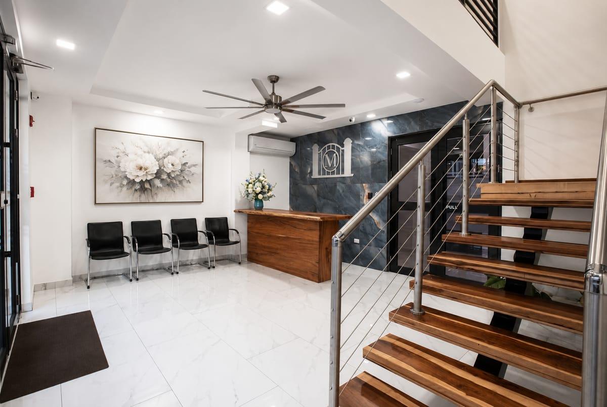 Morgan's Funeral Home reception lobby — wood desk with floral arrangement against the slate M emblem wall, with the wood floating staircase to the right